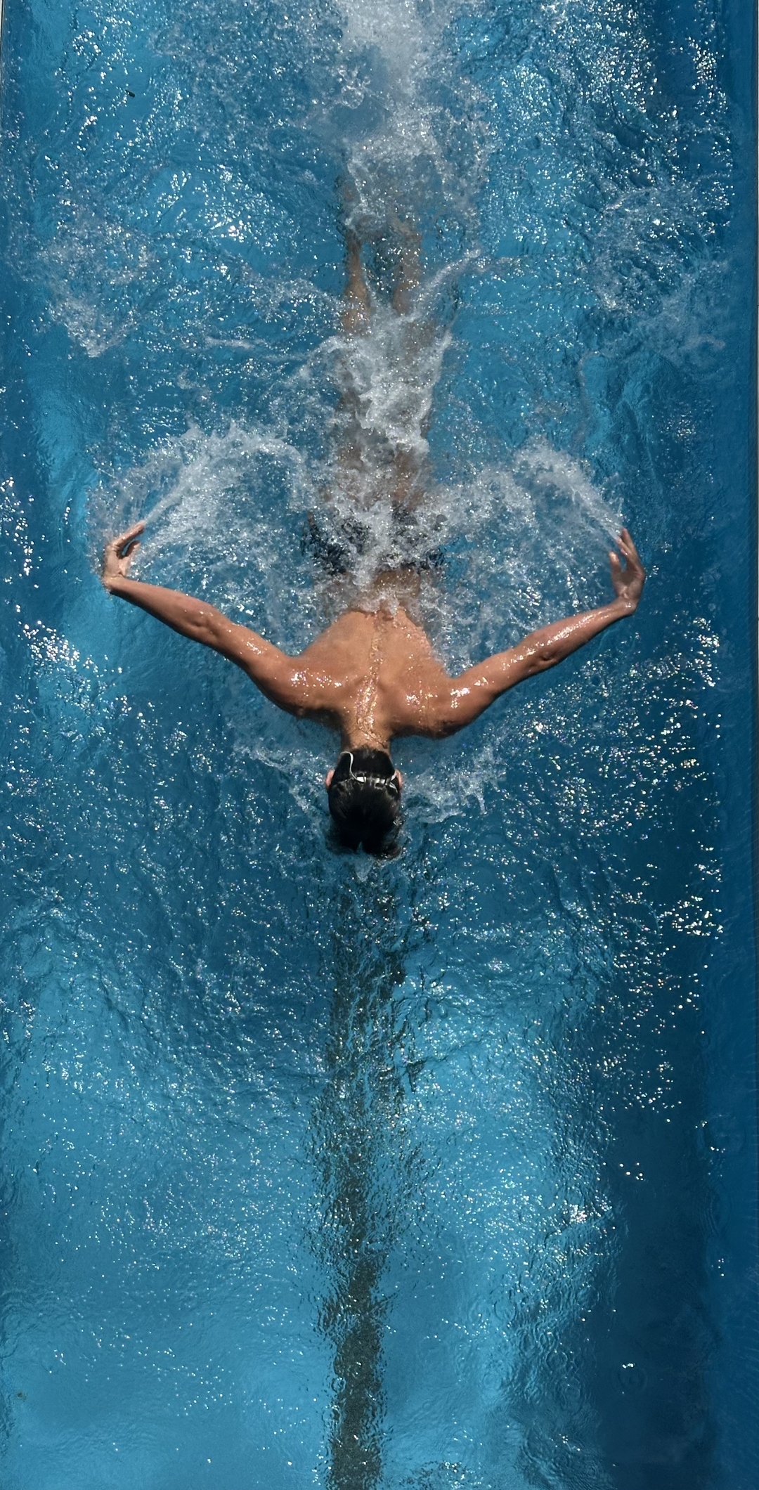 Overhead view of a swimmer mid-stroke, arms sweeping through clear aqua water in a single lane.
